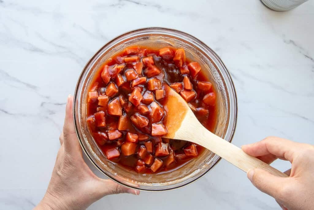 The cascos de guayaba are folded into the guava sauce in a glass mixing bowl.