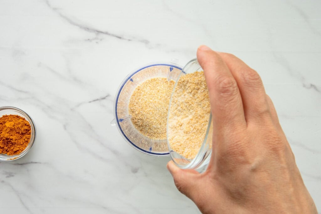 Pouring granulated onion powder into a spice mill.
