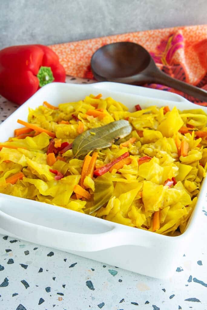 Caribbean Steamed Cabbage in a white square serving dish is garnished with a bay leaf.