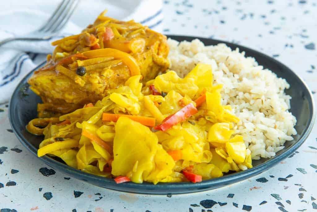 Caribbean Steamed Cabbage served on a dark plate with coconut rice and curry fish.