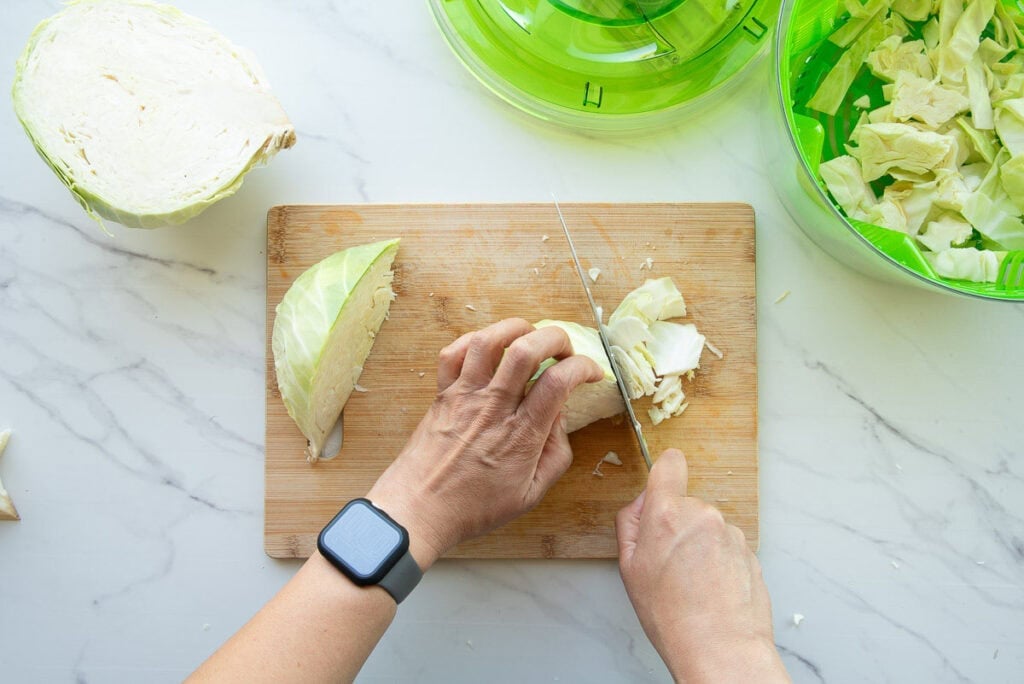 Hands cutting a wedge of green cabbage on a wooden cutting board.