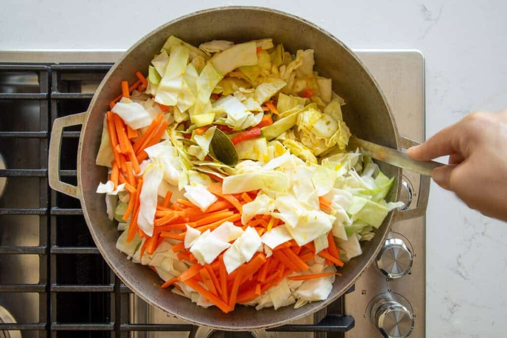 The cabbage and carrots are folded into the ingredients in a pot.