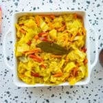 Caribbean Steamed Cabbage in a square serving dish next to a dark wooden serving spoon and an orange kitchen towel.