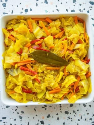 Caribbean Steamed Cabbage in a square serving dish next to a dark wooden serving spoon and an orange kitchen towel.