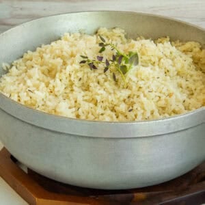 Caribbean Coconut Rice in a caldero is garnished with a sprig of fresh thyme.