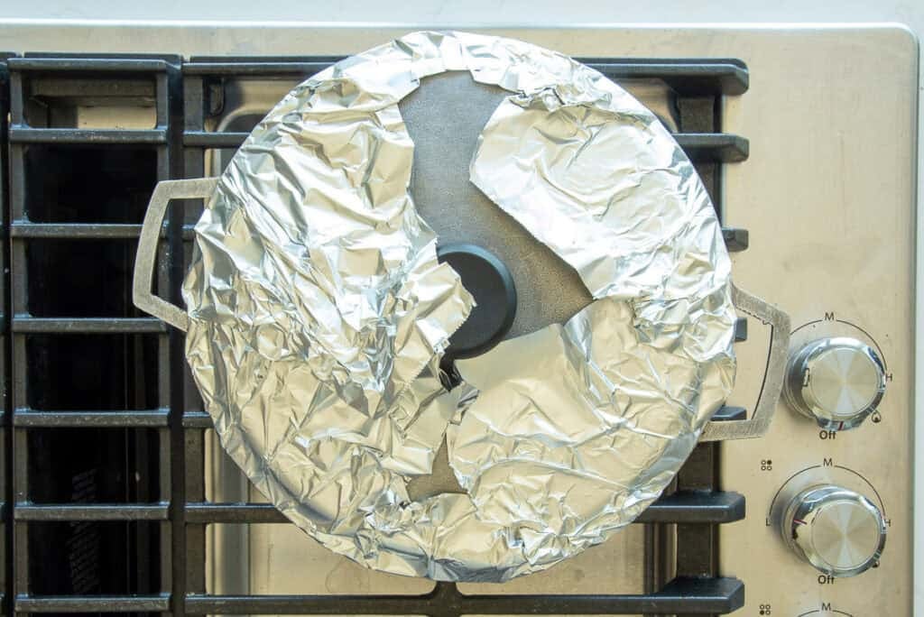 A foil-lined lid is on the caldero of rice which is on the stove.