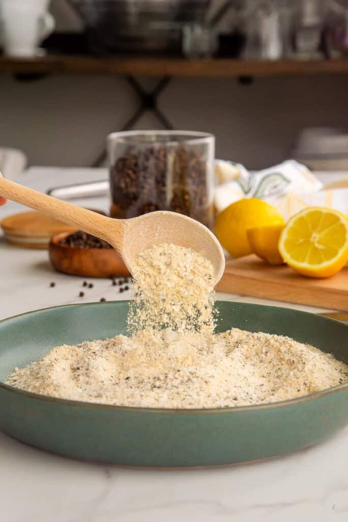 A spoon sprinkles the seasoning back into a green bowl with the rest of it.