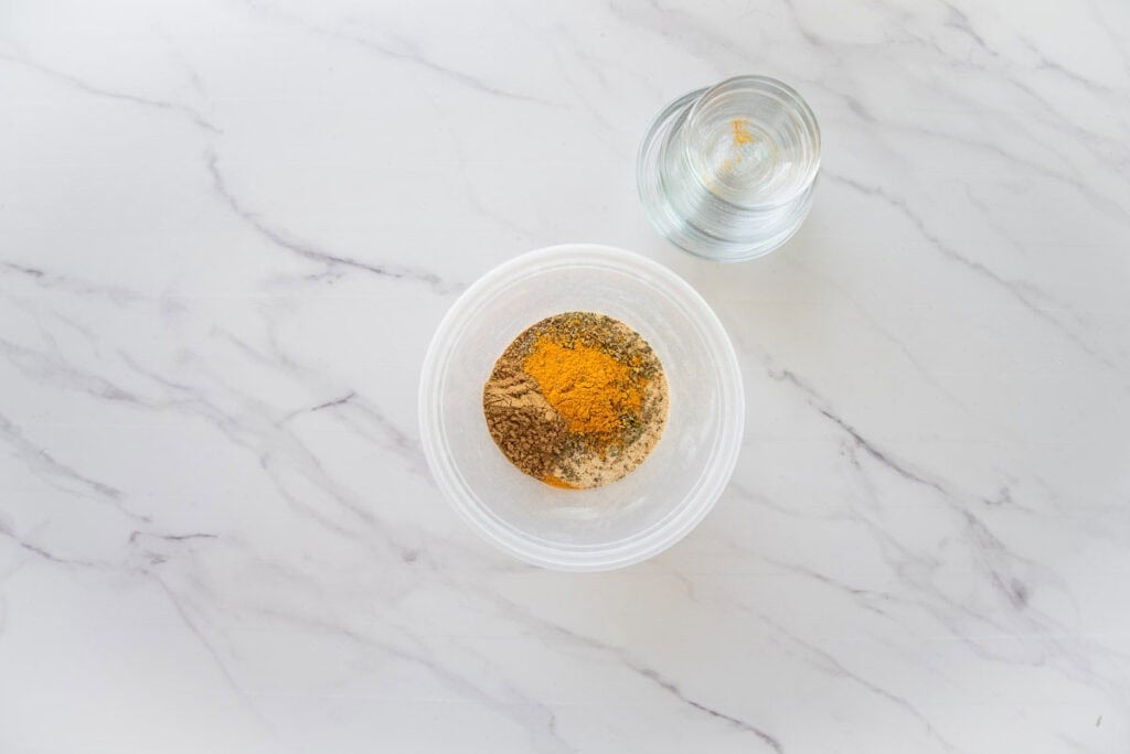 All of the herbs and spices are added to a plastic food container prior to mixing.