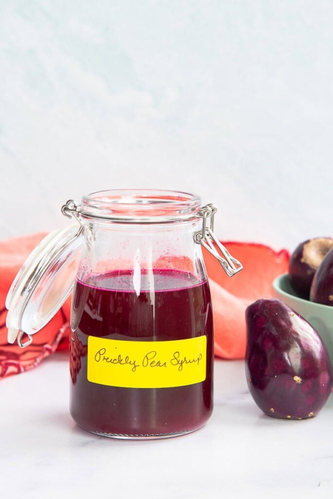 Prickly pear syrup in a glass jar next to a single prickly pear.