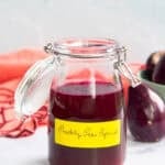 A glass jar holds prickly pear syrup and sits next to a prickly pear and a coral kitchen towel.