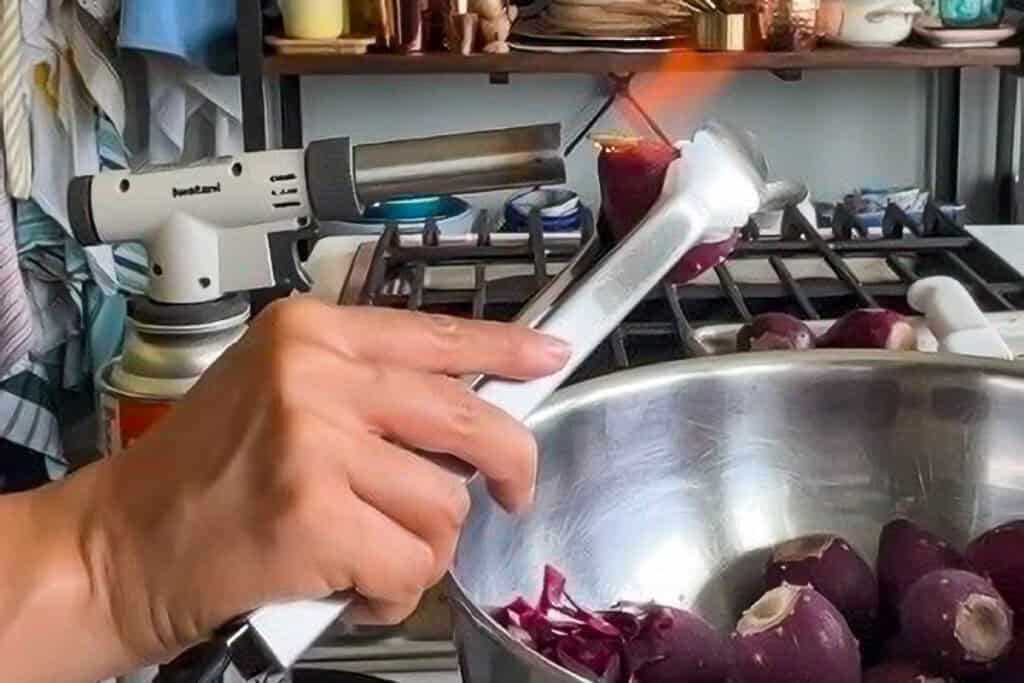 Marta holds a prickly pear up to the flame of a butane torch using tongs.