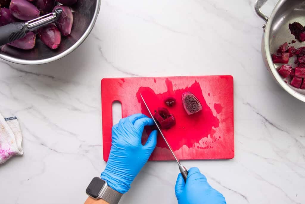 Marta uses a chefs knife to cut the peeled fruit into chunks on a red cutting board before adding the chunks to a pot.