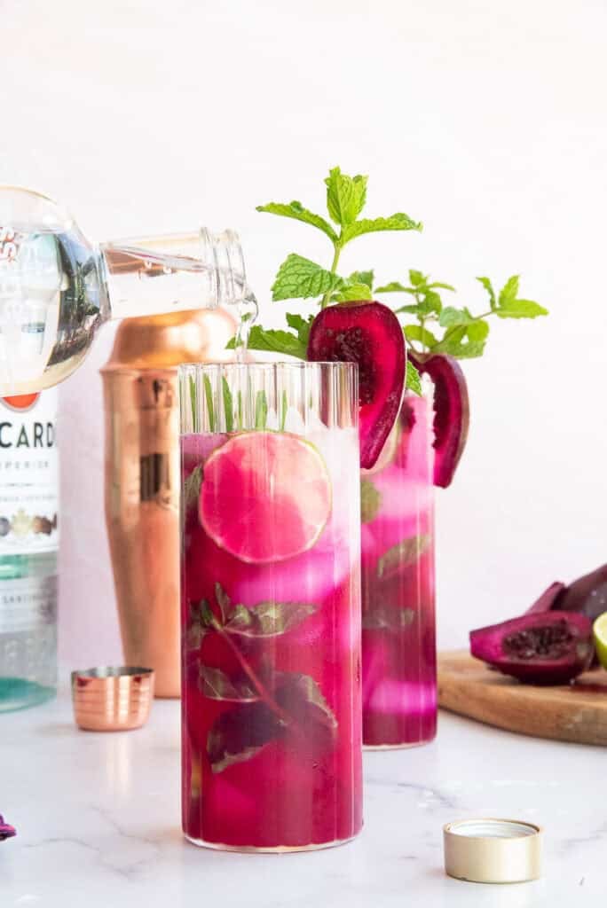 Sparkling soda is poured over the prickly pear mojito recipe in a highball glass.