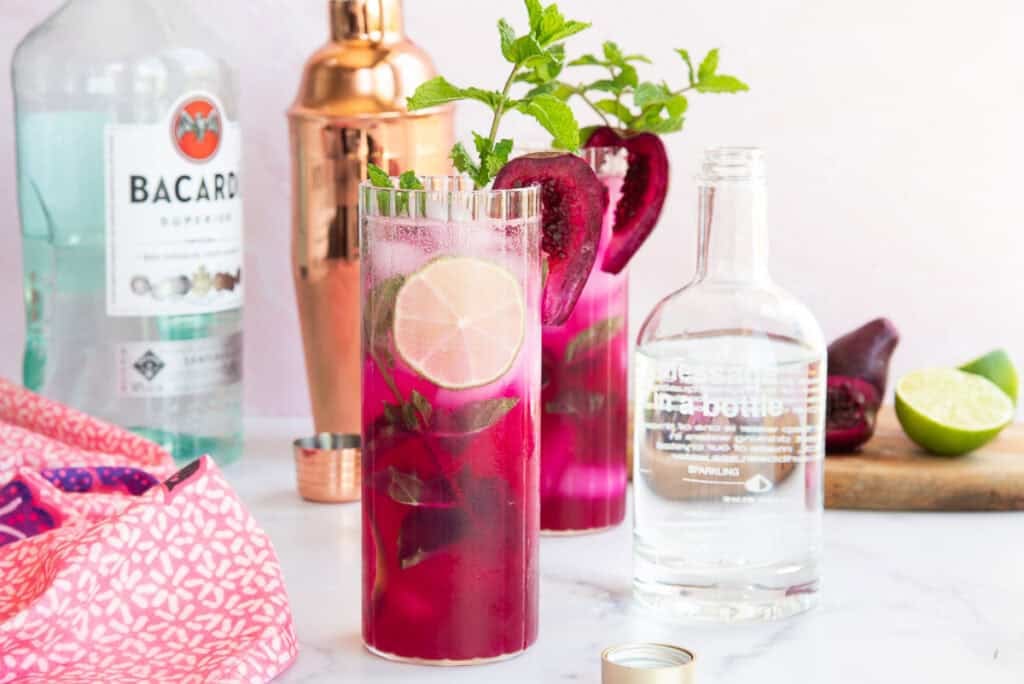 Two cocktail glasses filled with prickly pear mojitos, ice, and fresh mint.