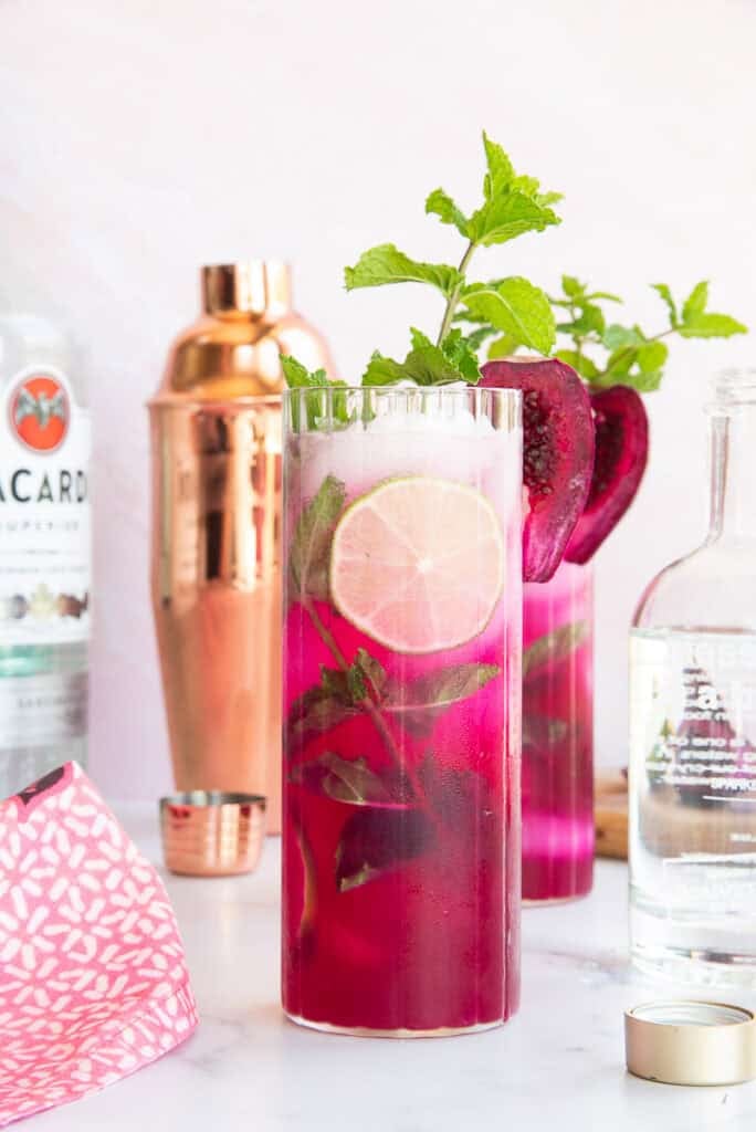 Prickly pear mojitos in a highball glass garnished with fresh mint, lime wheels, and prickly pear slices.