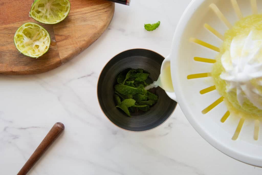 Lime juice is poured from a juicer into the cocktail shaker over the fresh mint leaves.